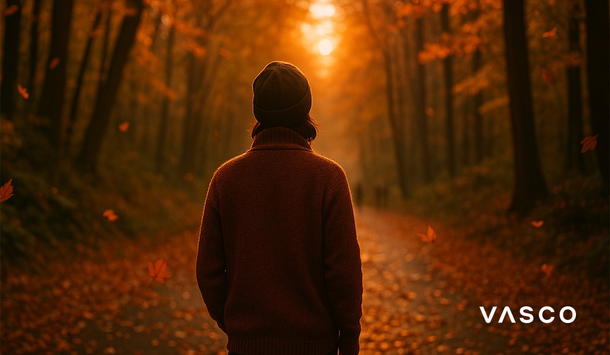 Osoba u smeđem džemperu hoda kroz šumu s opadajućim lišćem